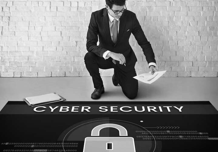 A man in a suit kneels on one knee, holding papers next to a clipboard. He faces a floor graphic with CYBER SECURITY and a padlock icon, highlighting IT security awareness for Portland businesses.
